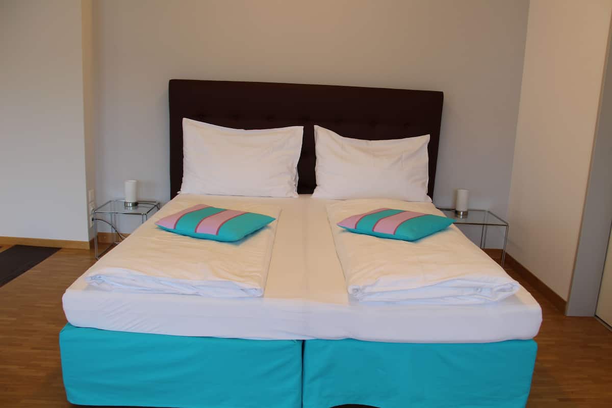 Een tweepersoonsbed met wit- en teal beddengoed, twee kussens en een donker hoofdbord.