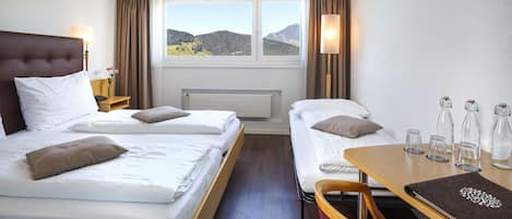 Habitación de hotel con dos camas, una mesa con vasos y vistas a las montañas.