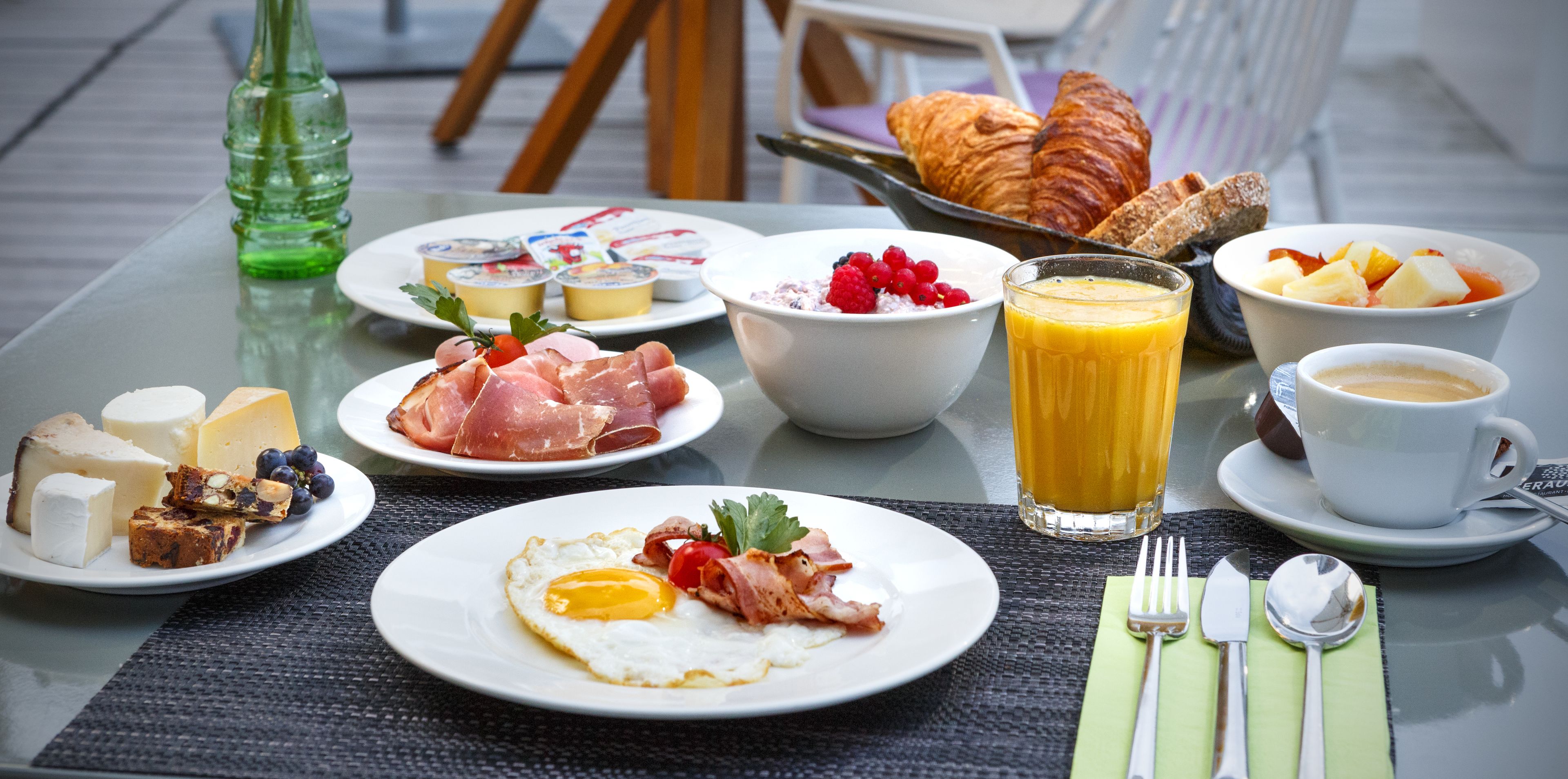 A breakfast table with plates of food, including eggs, ham, cheese, and croissants.