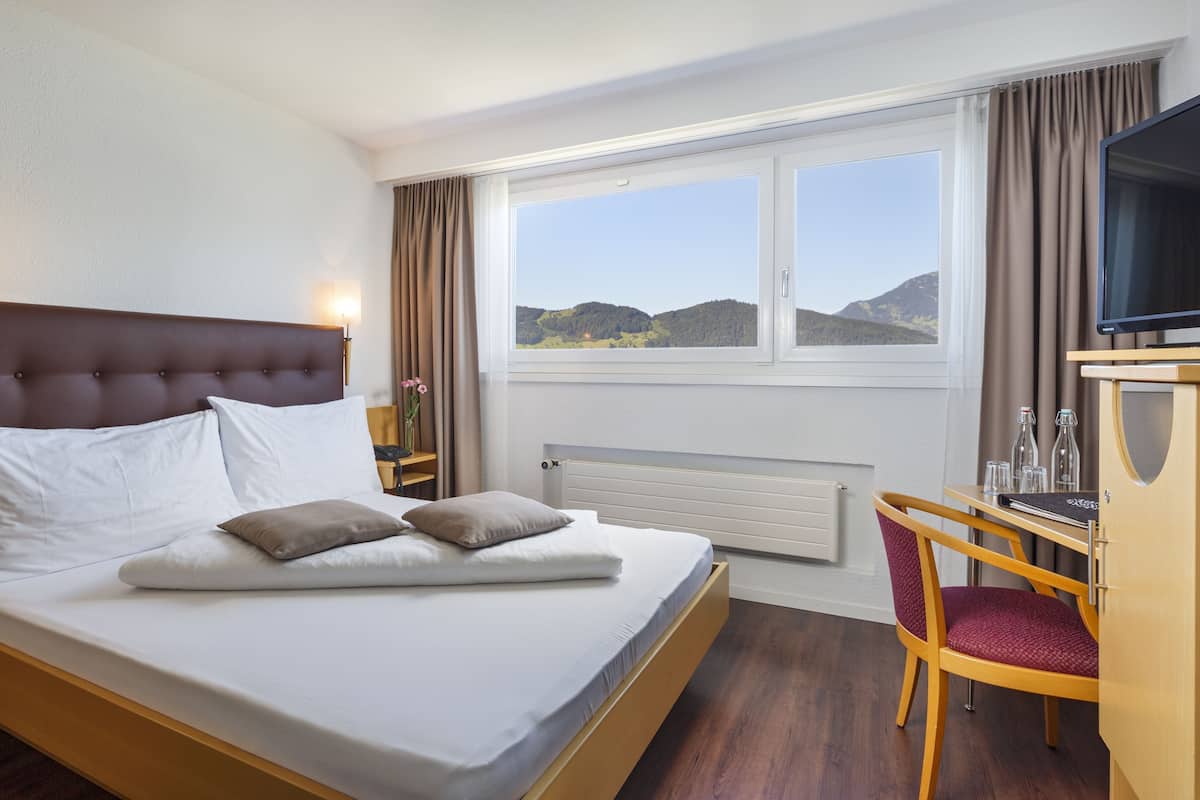 Hotelkamer met een bed, bureau, stoel, televisie en raam met uitzicht op heuvels.