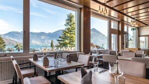 Ein Restaurant mit großen Fenstern und Blick auf die Berge. Tische sind mit Weingläsern und Besteck gedeckt.