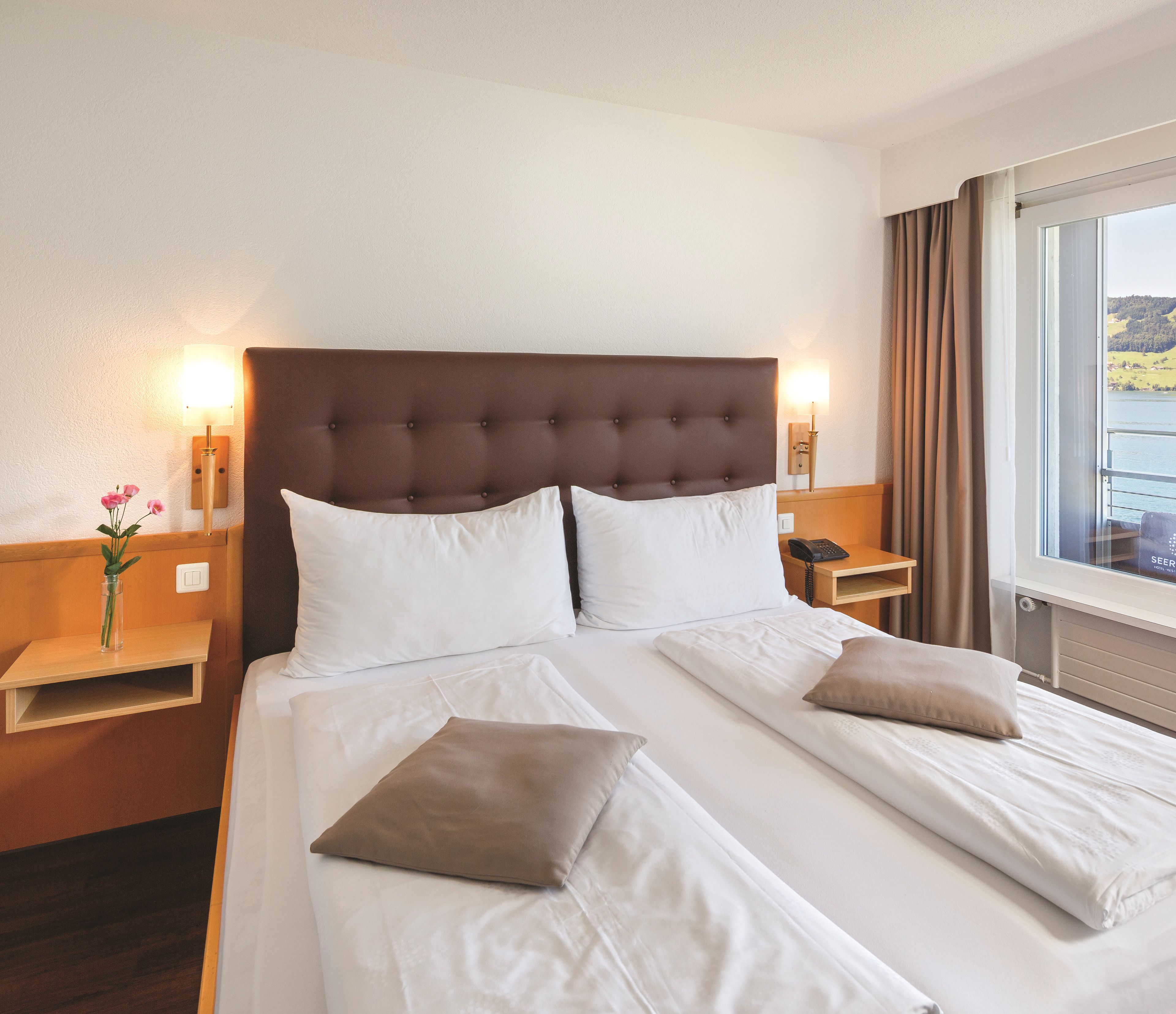 Habitación de hotel con una cama grande, dos mesitas de noche, una lámpara y una ventana con vistas.