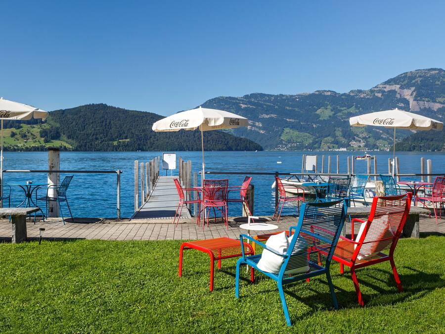 A lakeside terrace with outdoor seating, umbrellas, and a view of the water and hills.