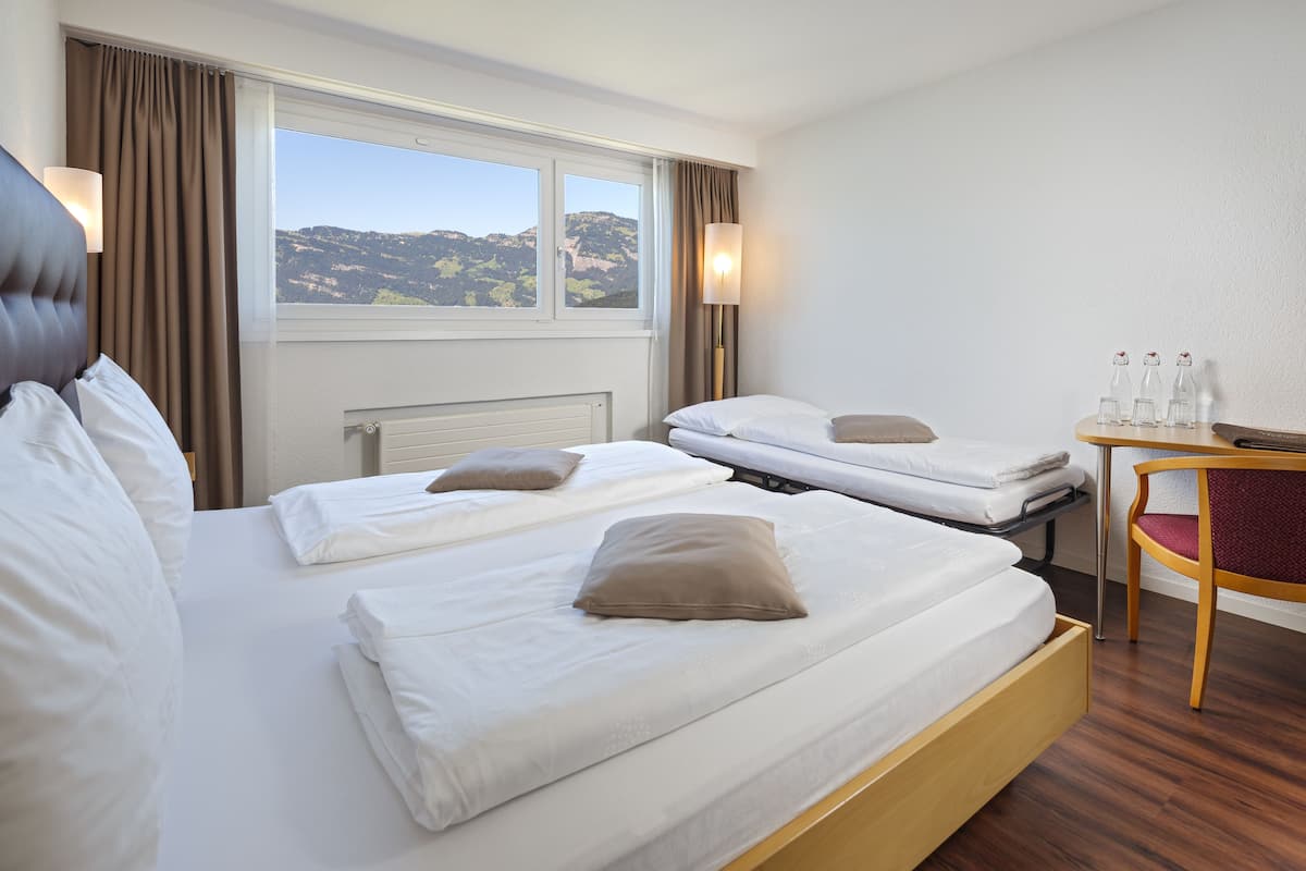 Een hotelkamer met twee bedden, een houten bureau en uitzicht op de bergen.