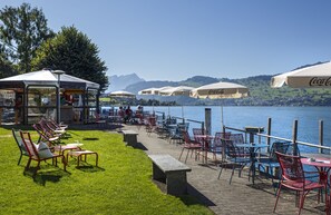 An outdoor seating area with tables and chairs, umbrellas, and a view of the lake. - Seerausch Swiss Quality Hotel (Beckenried)