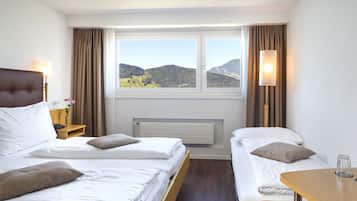 Une chambre d’hôtel avec deux lits, une vue sur les montagnes, un radiateur et une table avec un verre.