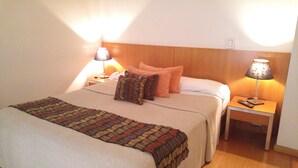 Een net opgemaakt bed met een geborduurd plaid, twee nachtkastjes met lampen, en een houten hoofdbord.