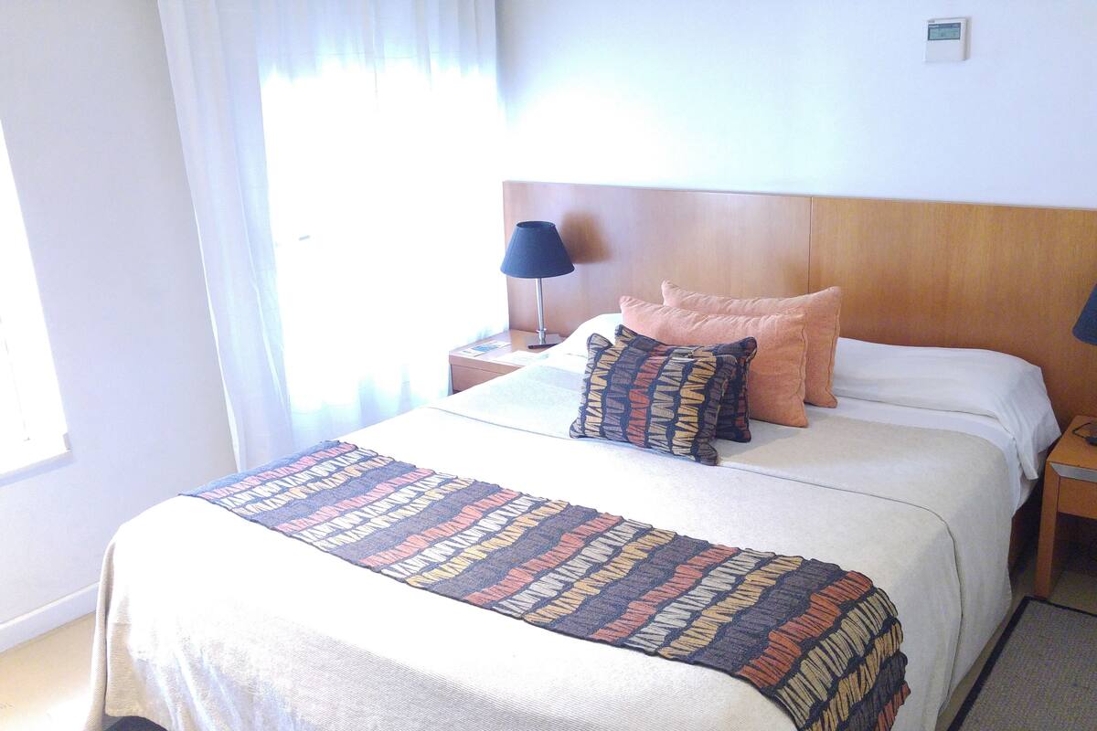 A neatly made bed with a patterned throw, two bedside lamps, and a nightstand with a phone.