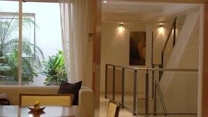 Een moderne hotellobby met een trap, een eetgedeelte met een tafel en stoelen, en een groot raam met planten.
