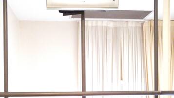 Una habitación con cama, un banco, un televisor montado en un soporte y una ventana con cortinas.