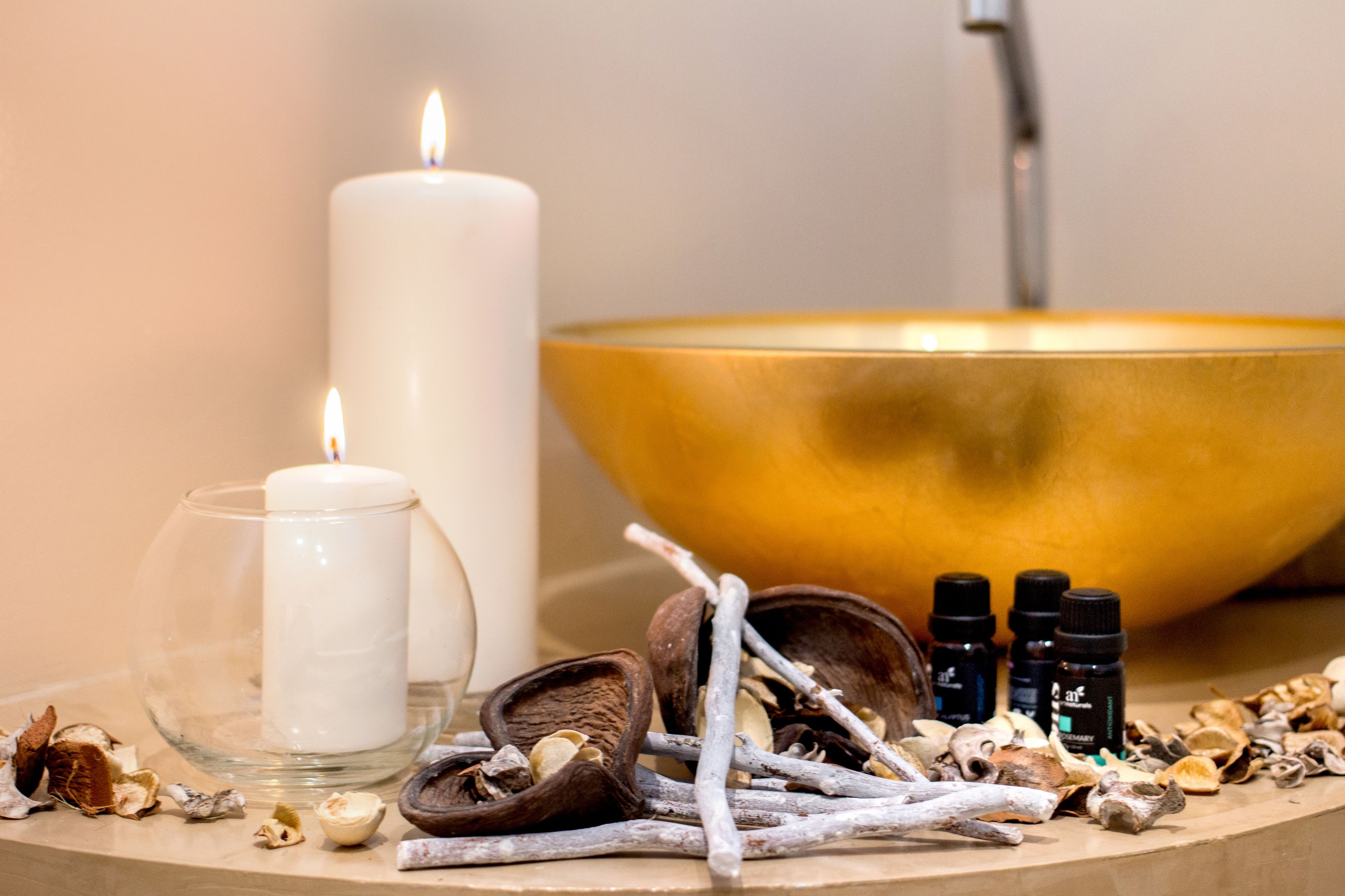 A candle, a golden bowl, and small bottles on a table.