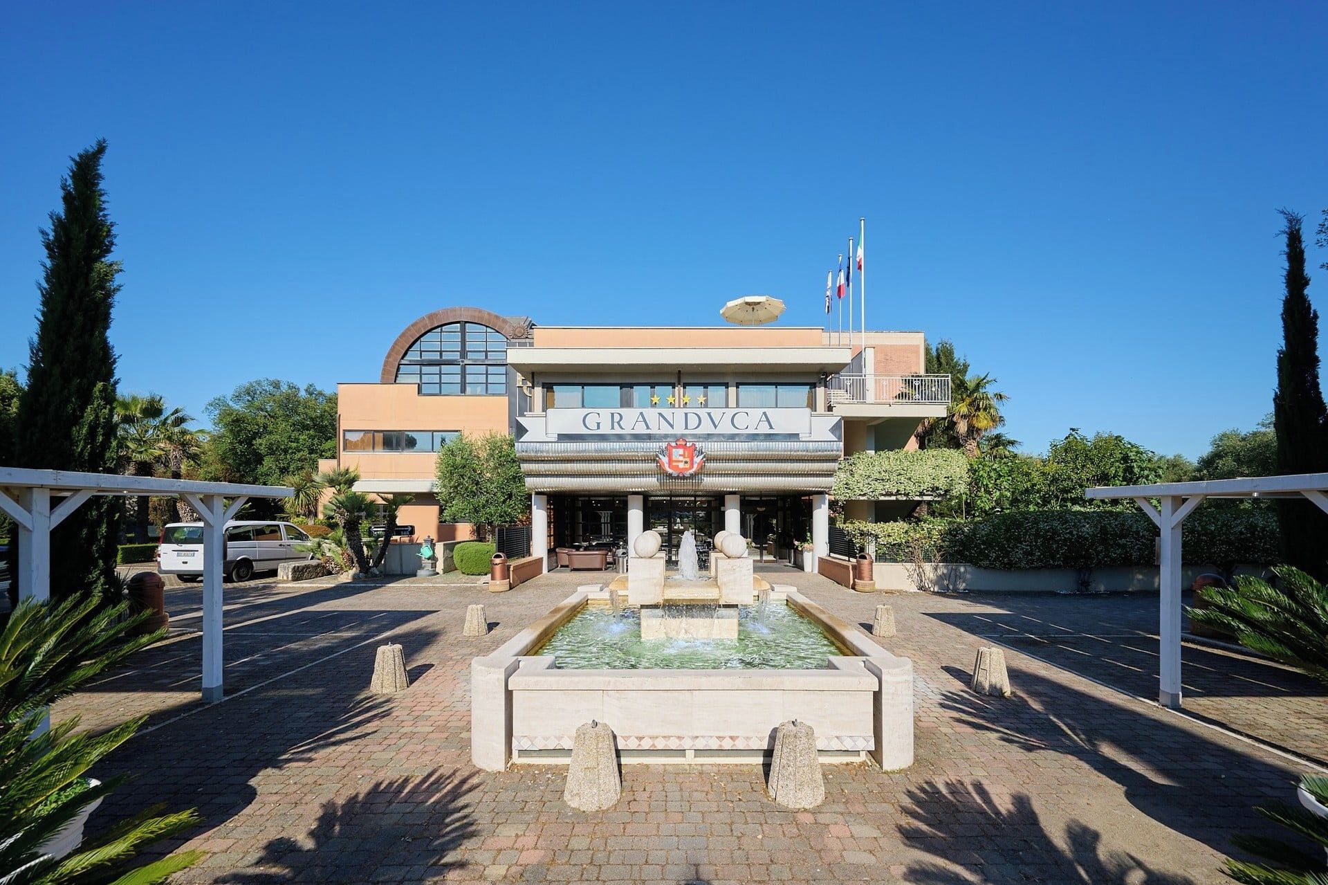 A hotel named GRANDVCA with a central fountain, surrounded by greenery and palm trees.