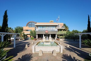 A hotel named GRANDVCA with a central fountain, surrounded by greenery and palm trees. - Granduca (Grosseto)