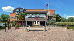 A hotel named GRANDVCA with a fountain in the center, surrounded by a paved area with potted plants. - Granduca (Grosseto)
