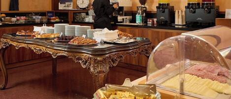 A buffet setup with various food items, a coffee station, and a clock on the wall.