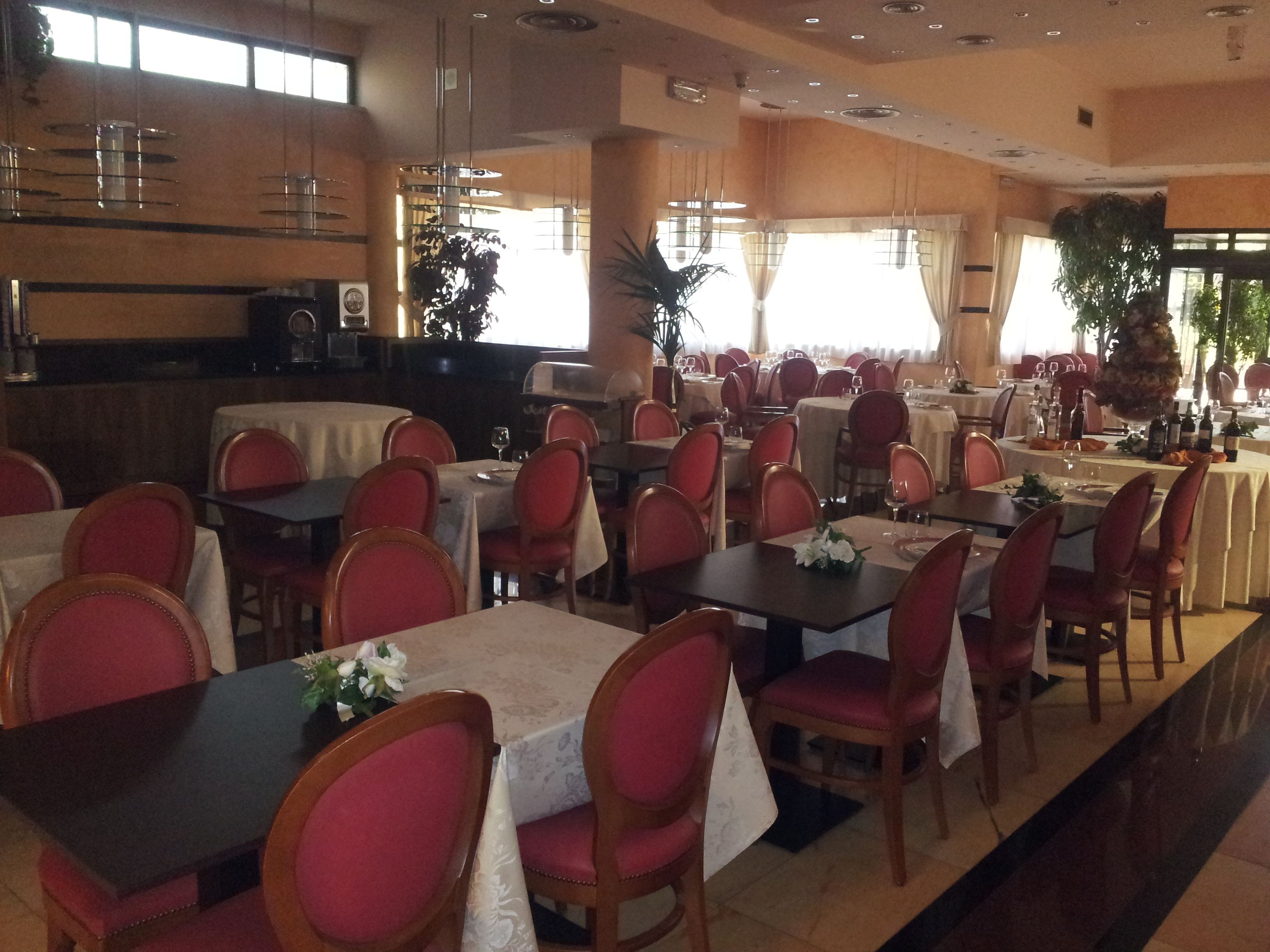 A restaurant with multiple tables and chairs, a kitchen area, and large windows allowing natural light.