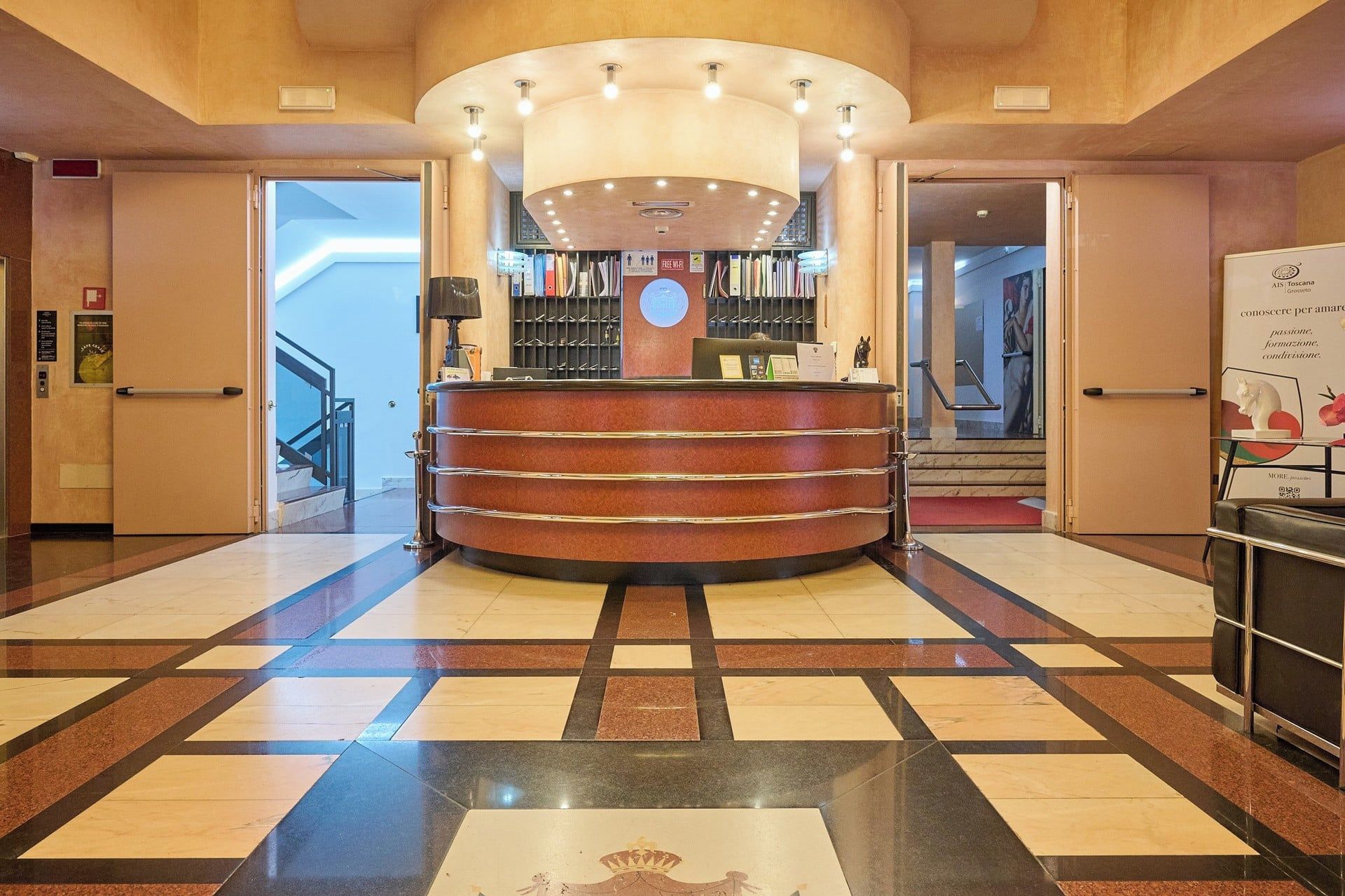 A hotel reception area with a curved desk, a clock, and a staircase leading to an upper floor.