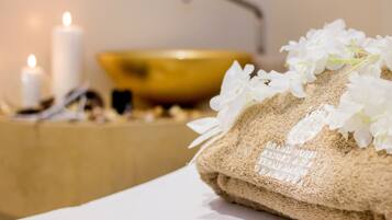 Ambiente de spa com toalha, flores brancas, velas e uma tigela dourada.