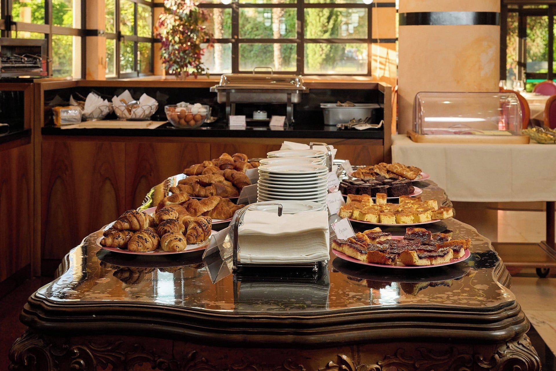 A buffet table with various pastries and desserts, a coffee machine, and a window with a view of greenery.