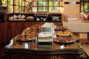 A buffet table with various pastries and desserts, a coffee machine, and a window with a view of greenery. - Granduca (Grosseto)