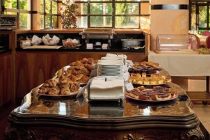 A buffet table with various pastries and desserts, a coffee machine, and a window with a view of greenery.