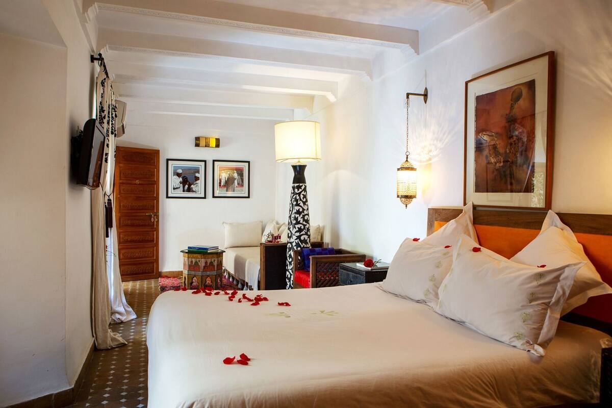 A hotel room with a large bed, a desk, a chair, a lamp, and a painting on the wall.