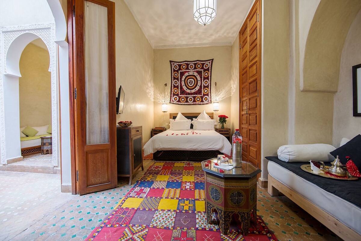 A traditional Moroccan room with a bed, a patterned rug, a wall hanging, and a wooden cabinet.