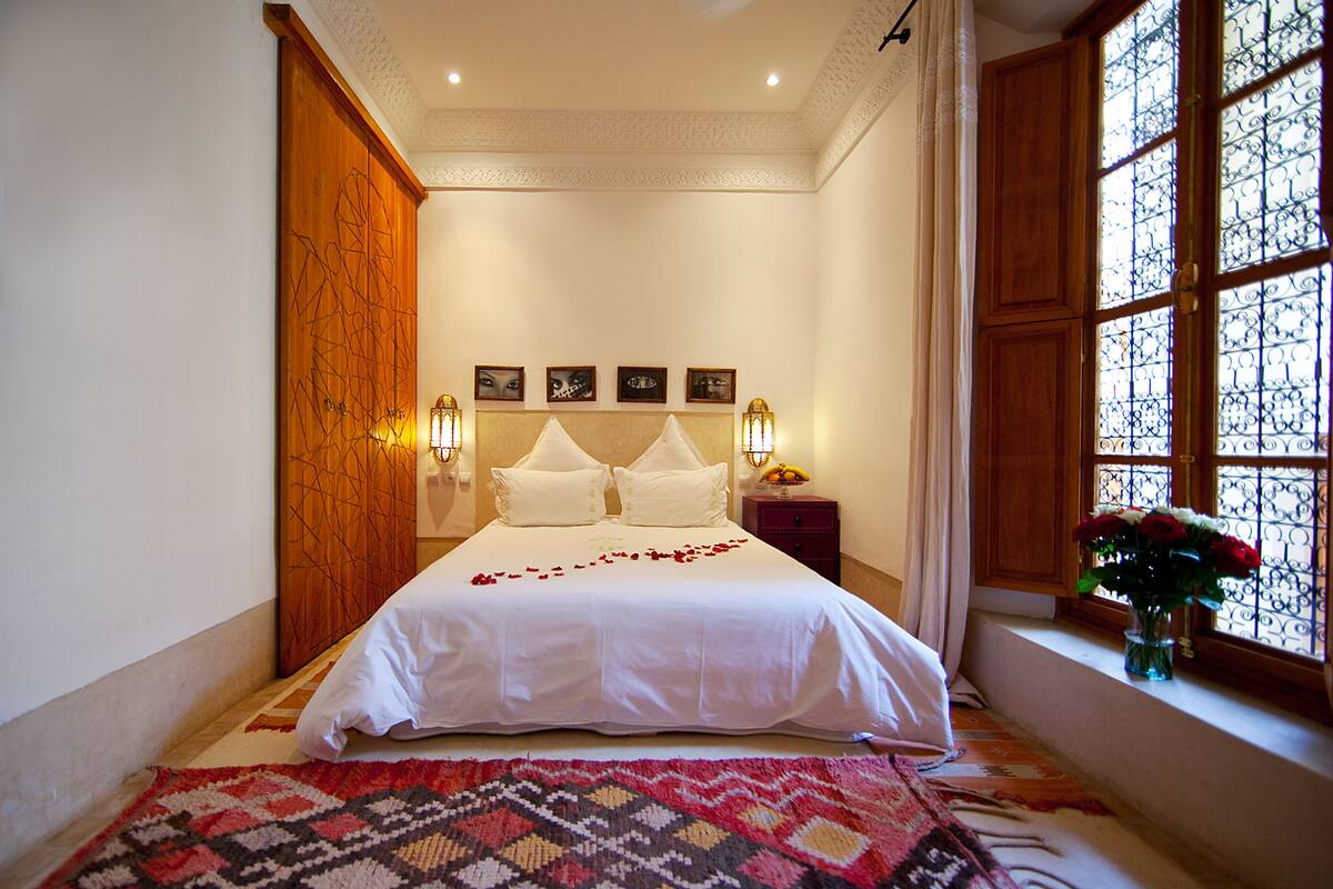 A neatly made bed with white linens, a patterned rug, and a nightstand with a lamp.