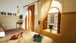 Habitación de hotel con cama, una mesita con lámpara, ventana con cortinas y vista a zonas verdes.