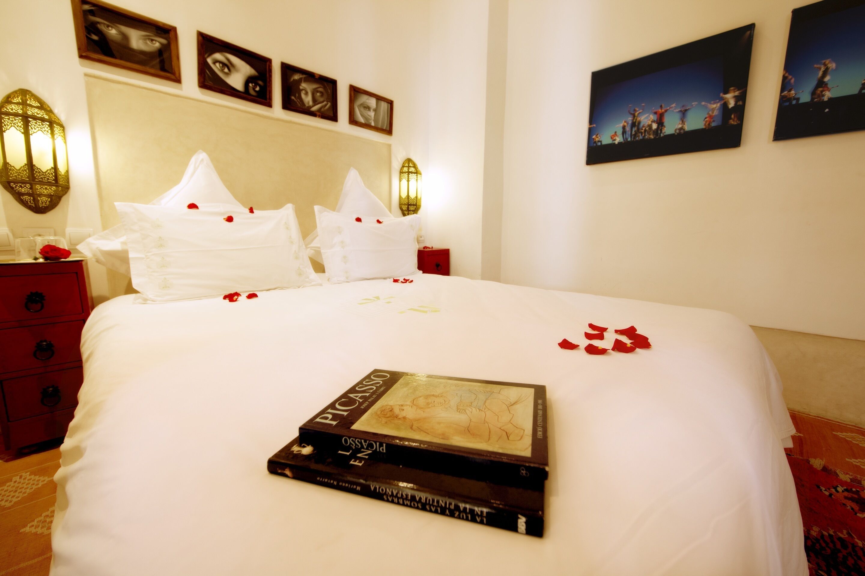 A neatly made bed with rose petals and a book titled "Picasso" on it.
