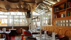 Un restaurante con mesas dispuestas para comer, una estantería con libros y un ventanal que deja entrar luz natural.