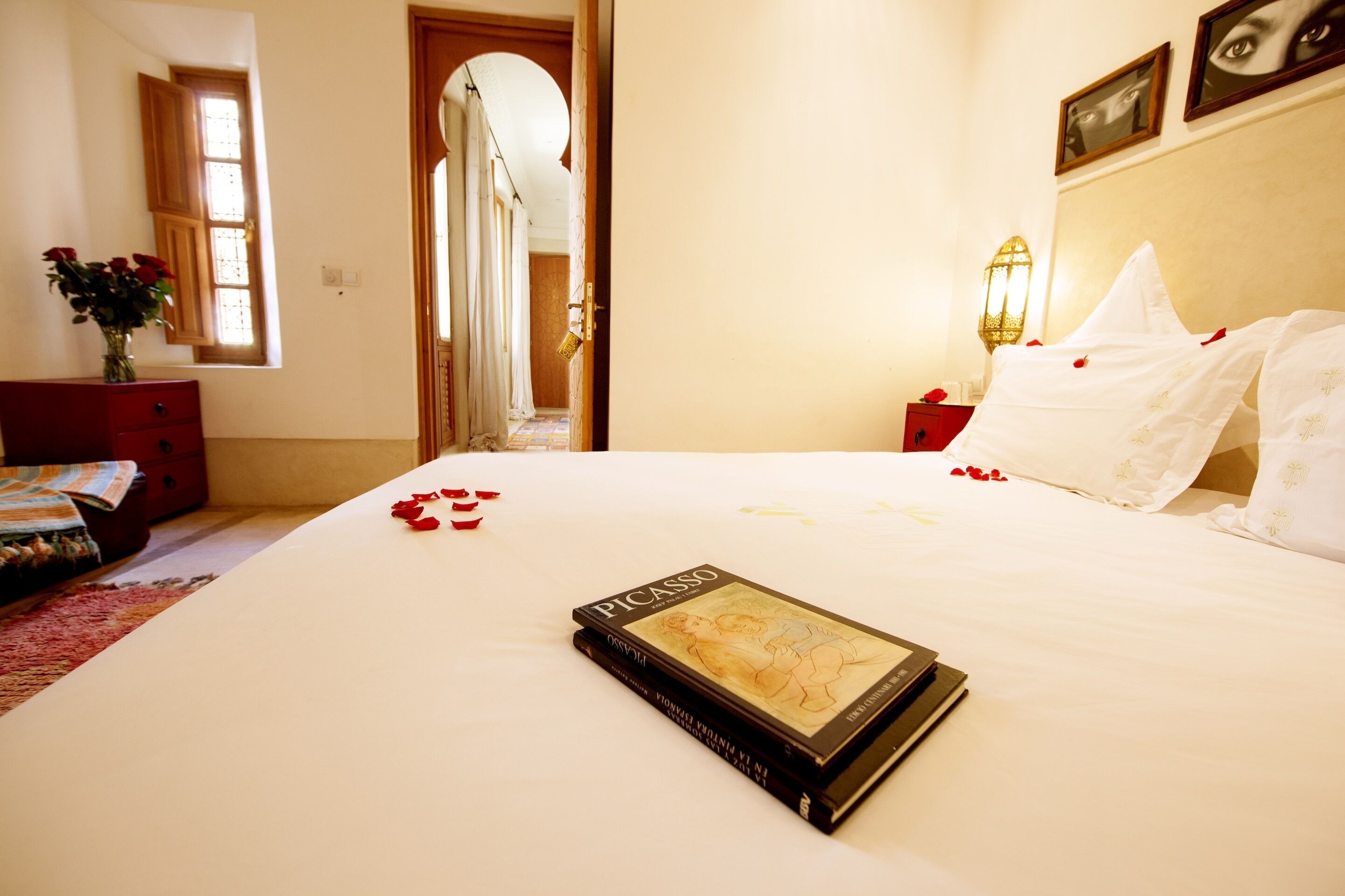 A neatly made bed with rose petals and a book titled "Picasso" on it.