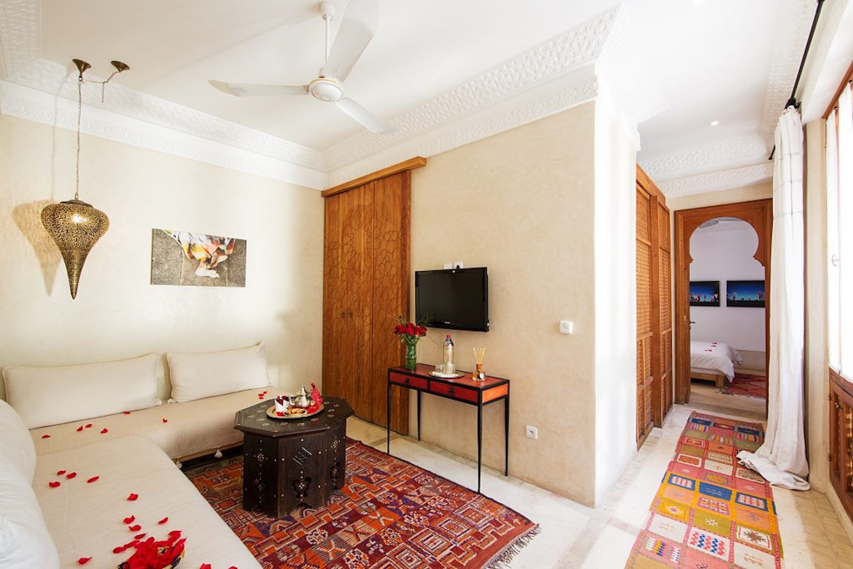 Una habitación de hotel con un sofá, una mesita con un florero y velas, un televisor y una alfombra colorida.