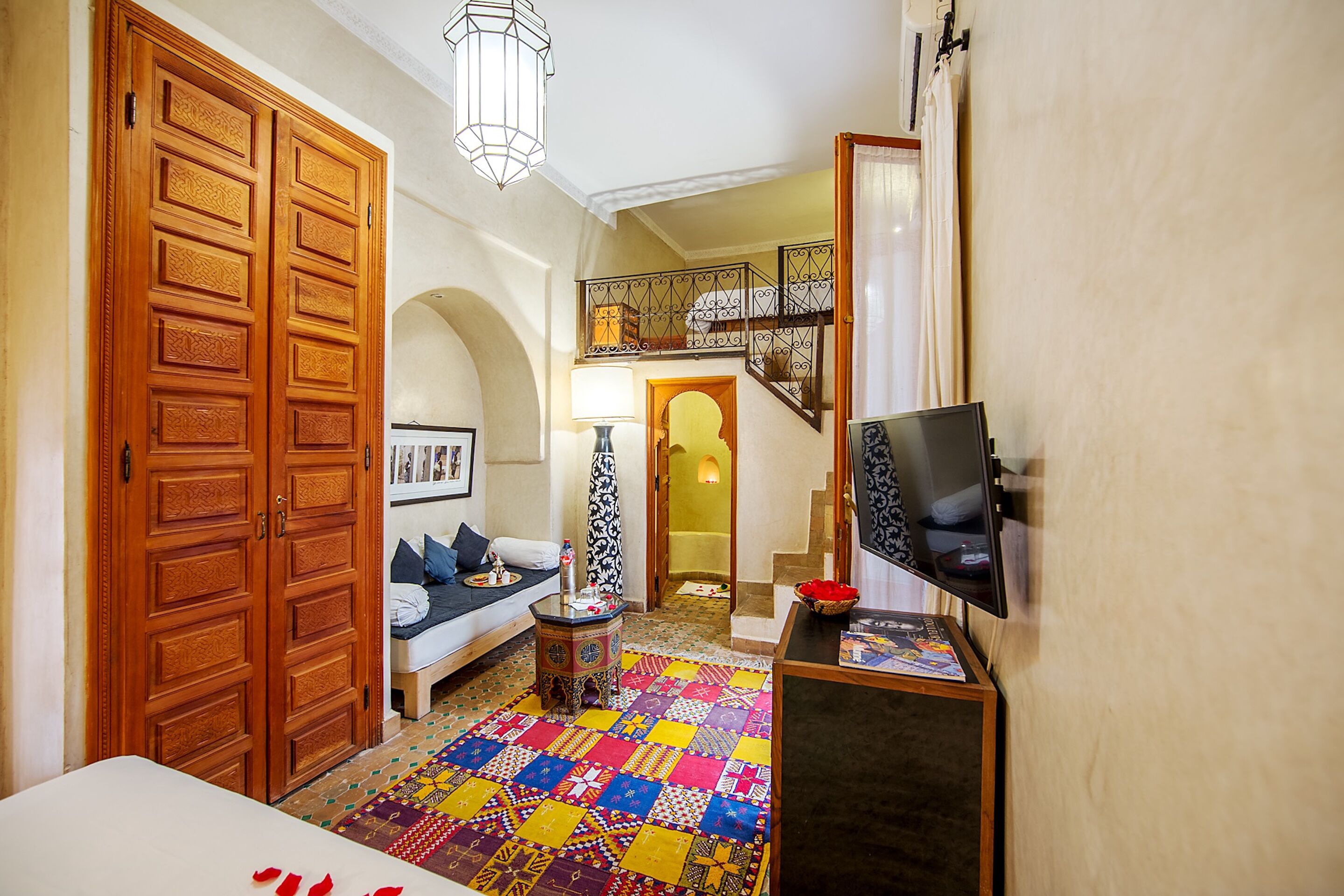 Una sala de estar acogedora con un suelo de patchwork colorido, un sofá con cojines, un televisor sobre un mueble bajo y una puerta de madera.