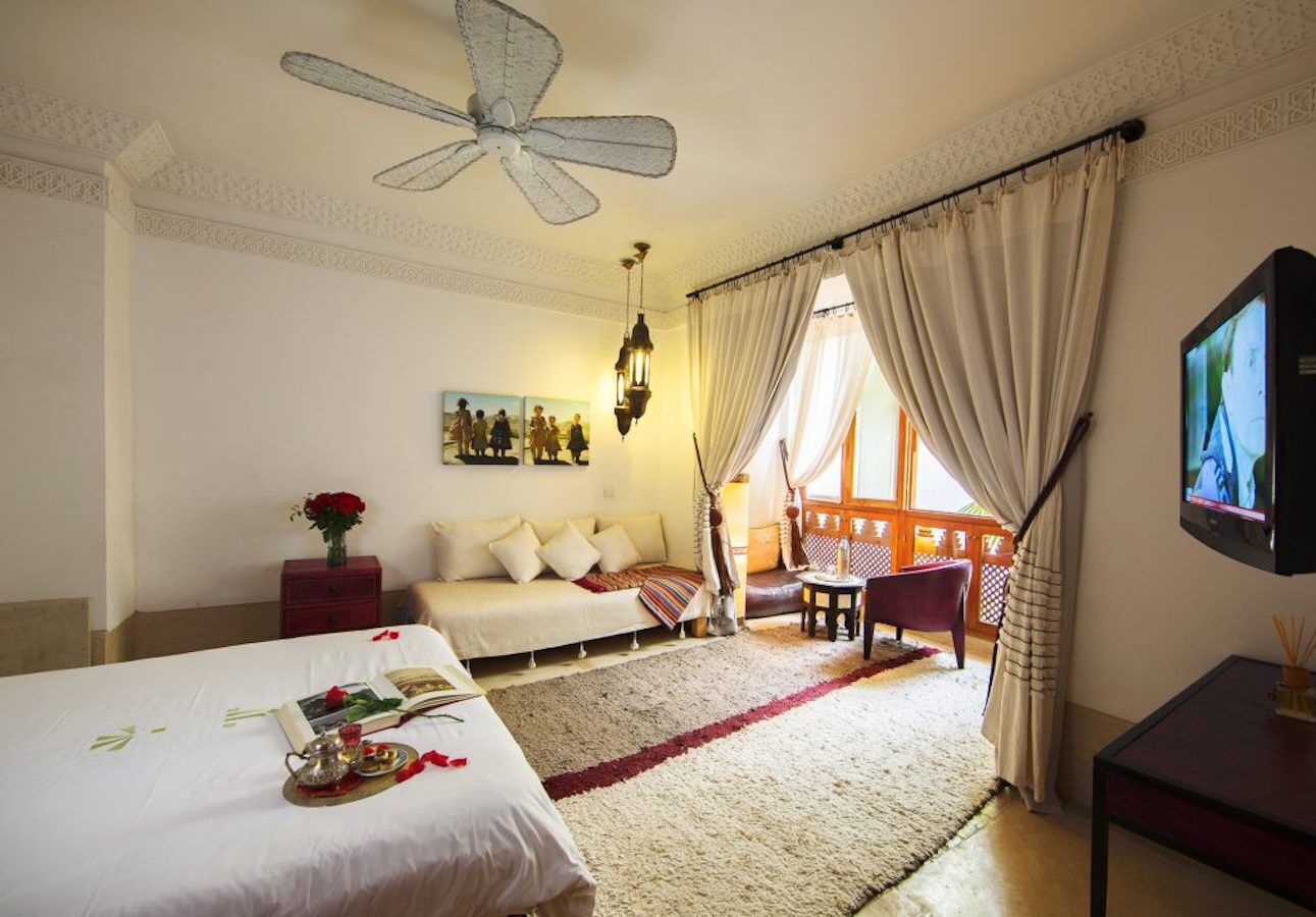 A hotel room with a bed, a sofa, a TV, and a balcony with curtains.
