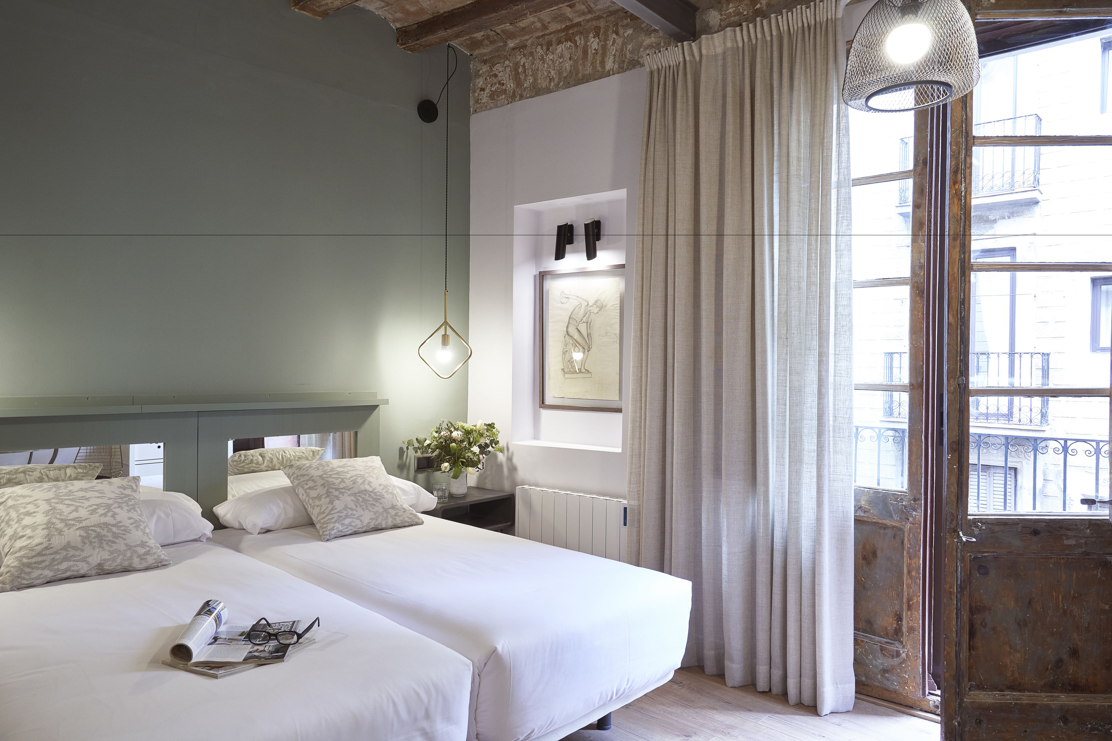 A hotel room with two beds, a window with curtains, a radiator, and a hanging light fixture.