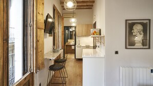 A narrow kitchen with wooden beams, a white countertop, and a hanging light fixture. - AinB Gothic-Jaume I Apartments (Barcelona)