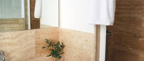 A bathroom with a sink, mirror, towel rack, shower, and a small plant on the counter.