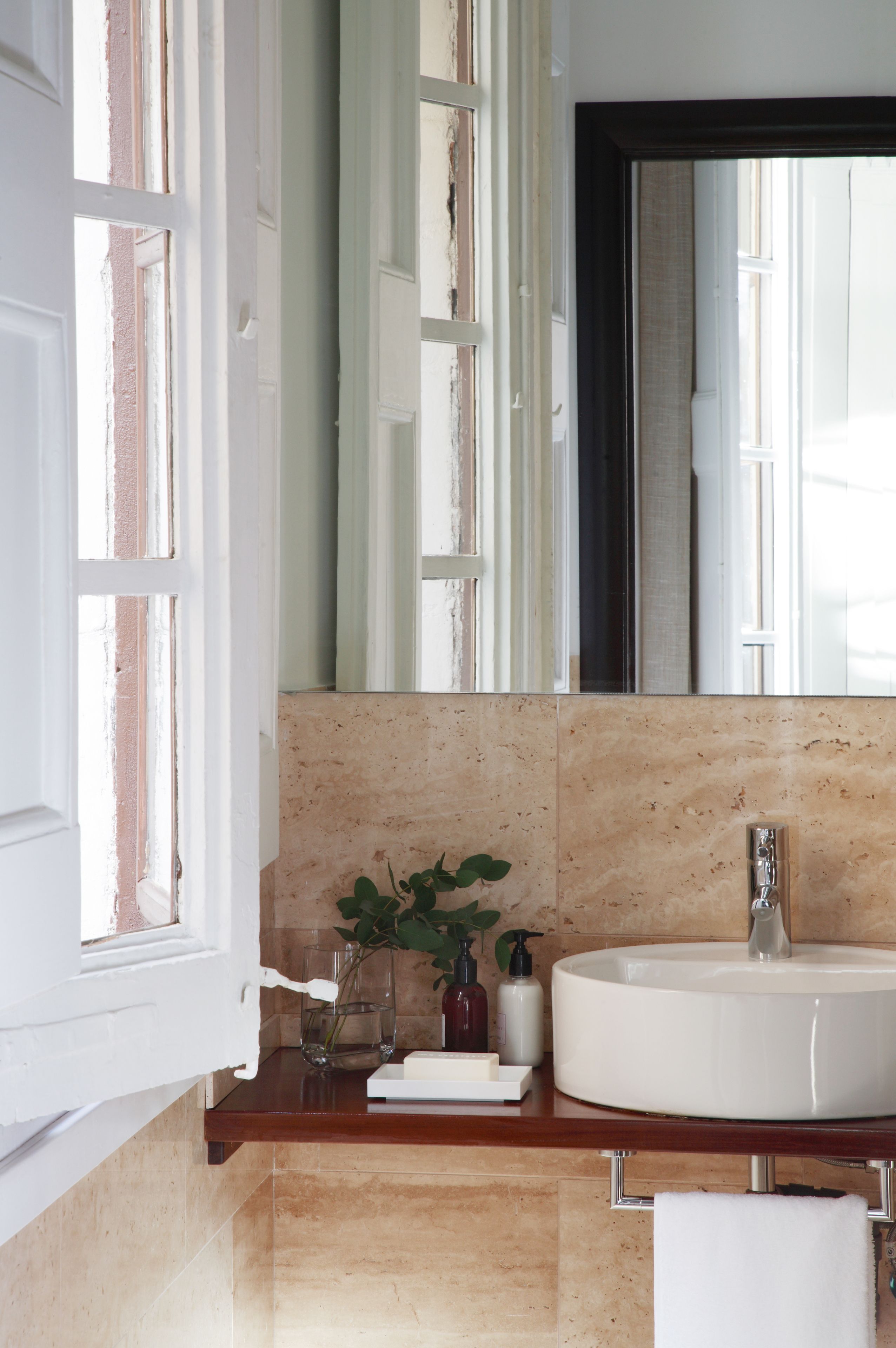 Une salle de bain avec un grand miroir, un lavabo rond et une fenêtre avec des rideaux.