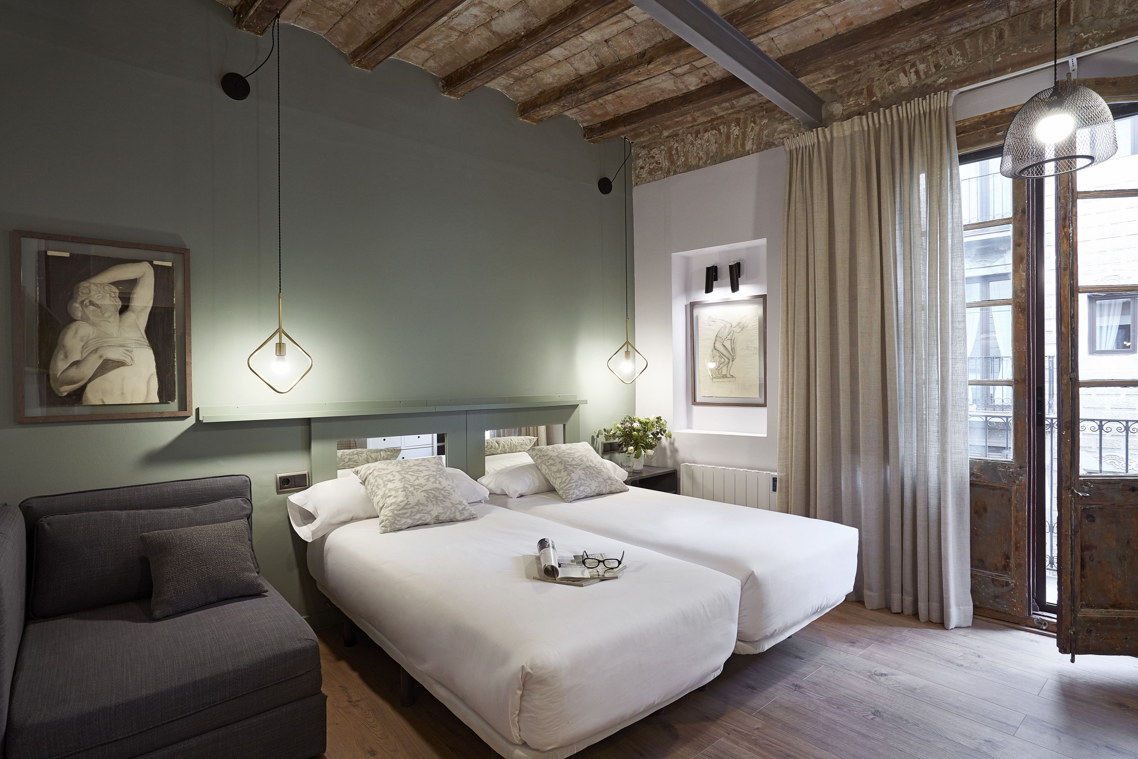 A hotel room with two beds, a sofa, a painting, and a view of the city.