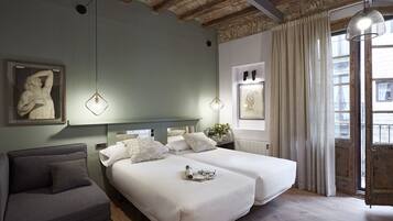 A hotel room with two beds, a sofa, a painting, and a view of the city.