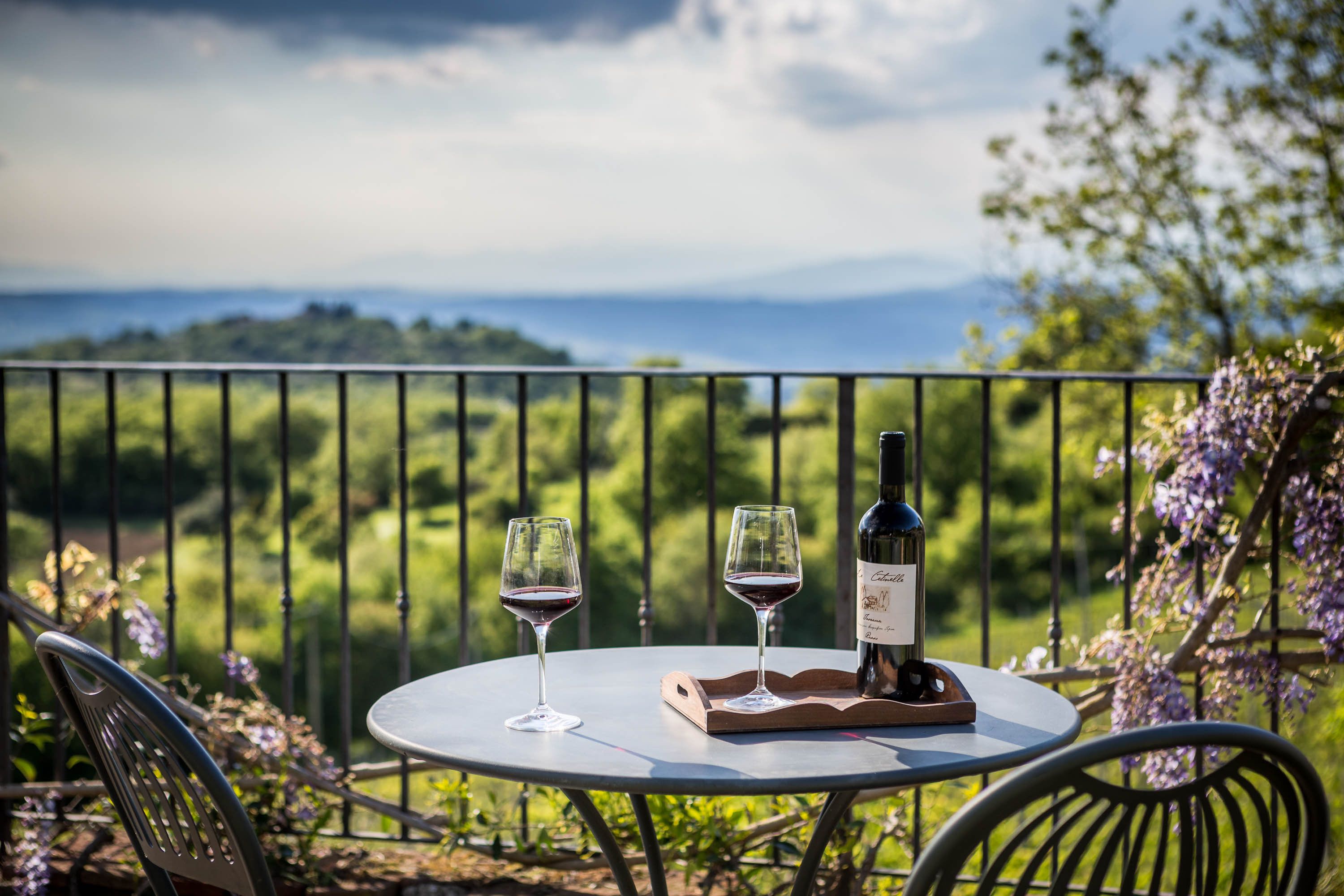 Ein runder Tisch mit zwei Weingläsern und einer Flasche auf einem Balkon mit Blick auf eine malerische Landschaft.