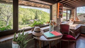 Una habitación acogedora con un gran ventanal, una mesa de madera, una silla roja, una estantería y una planta de cactus.