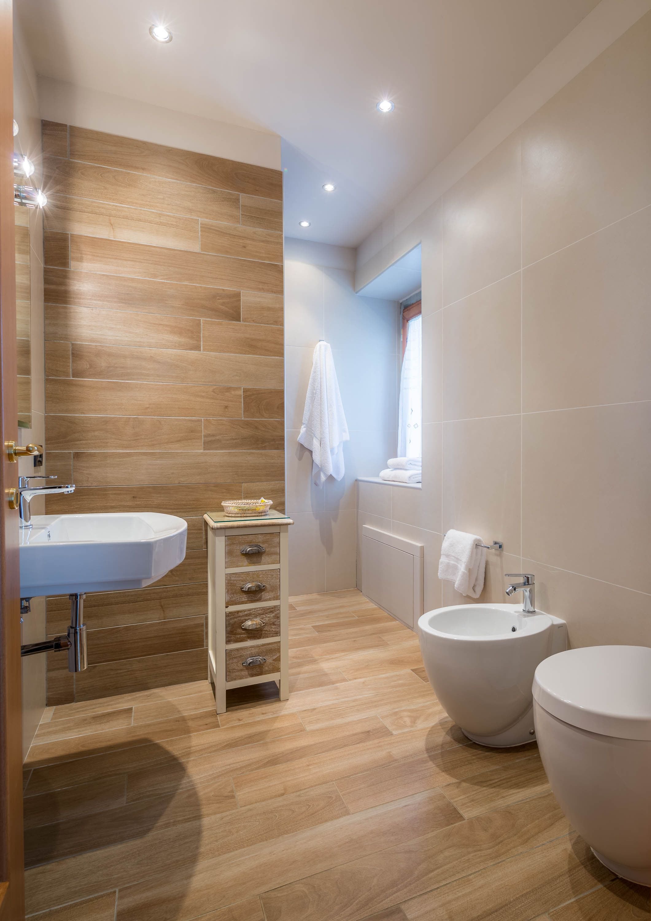Ein modernes Badezimmer mit Holzboden, einem weißen Waschbecken, einem Bidet und einer Toilette.