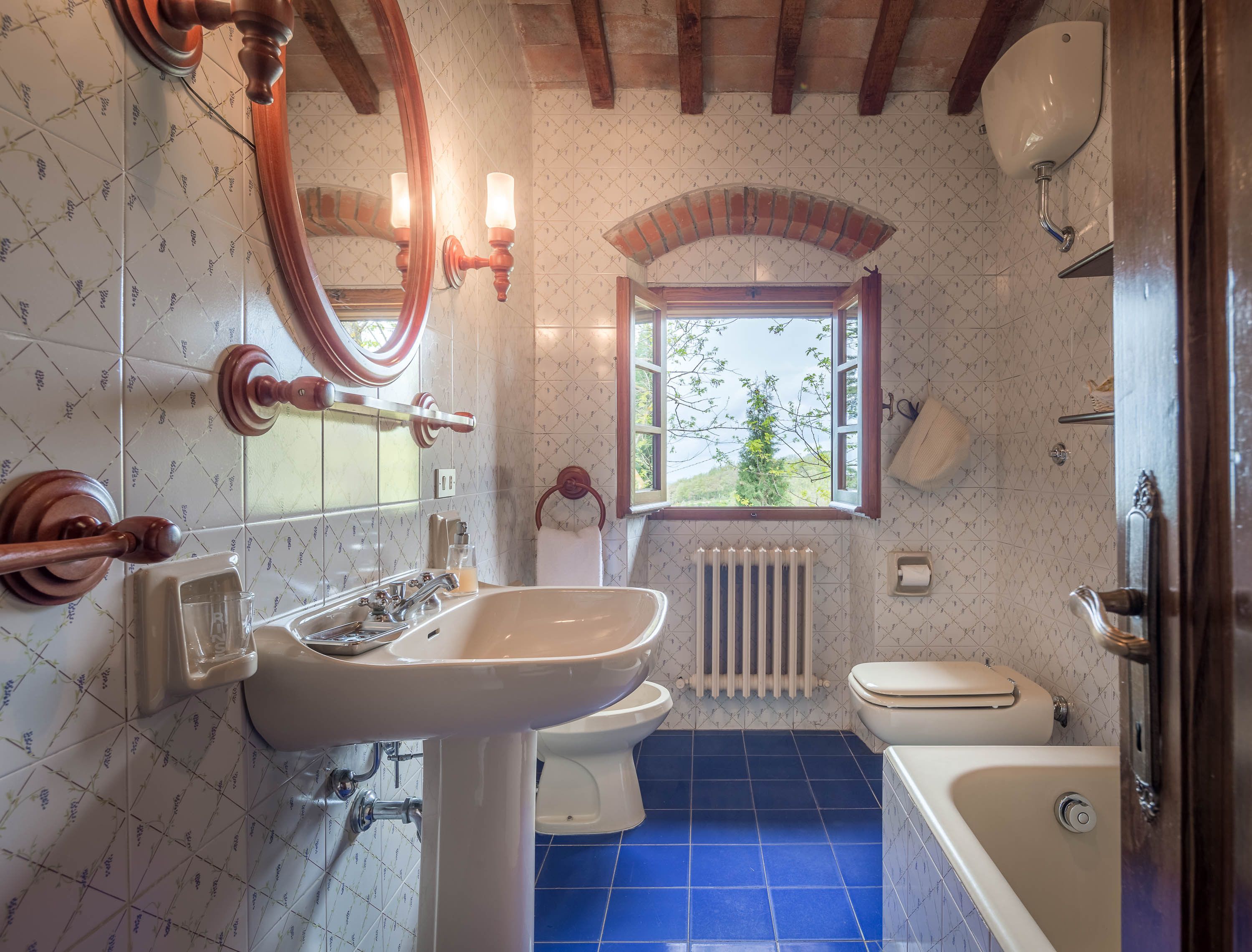 A bathroom with a bathtub, toilet, and sink, featuring patterned tiles and wooden fixtures.