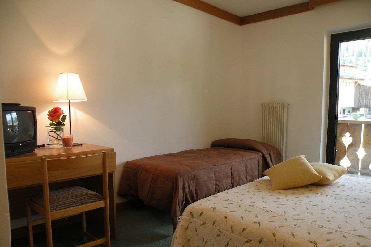 A hotel room with a bed, a desk with a lamp, a television, and a window with a view.