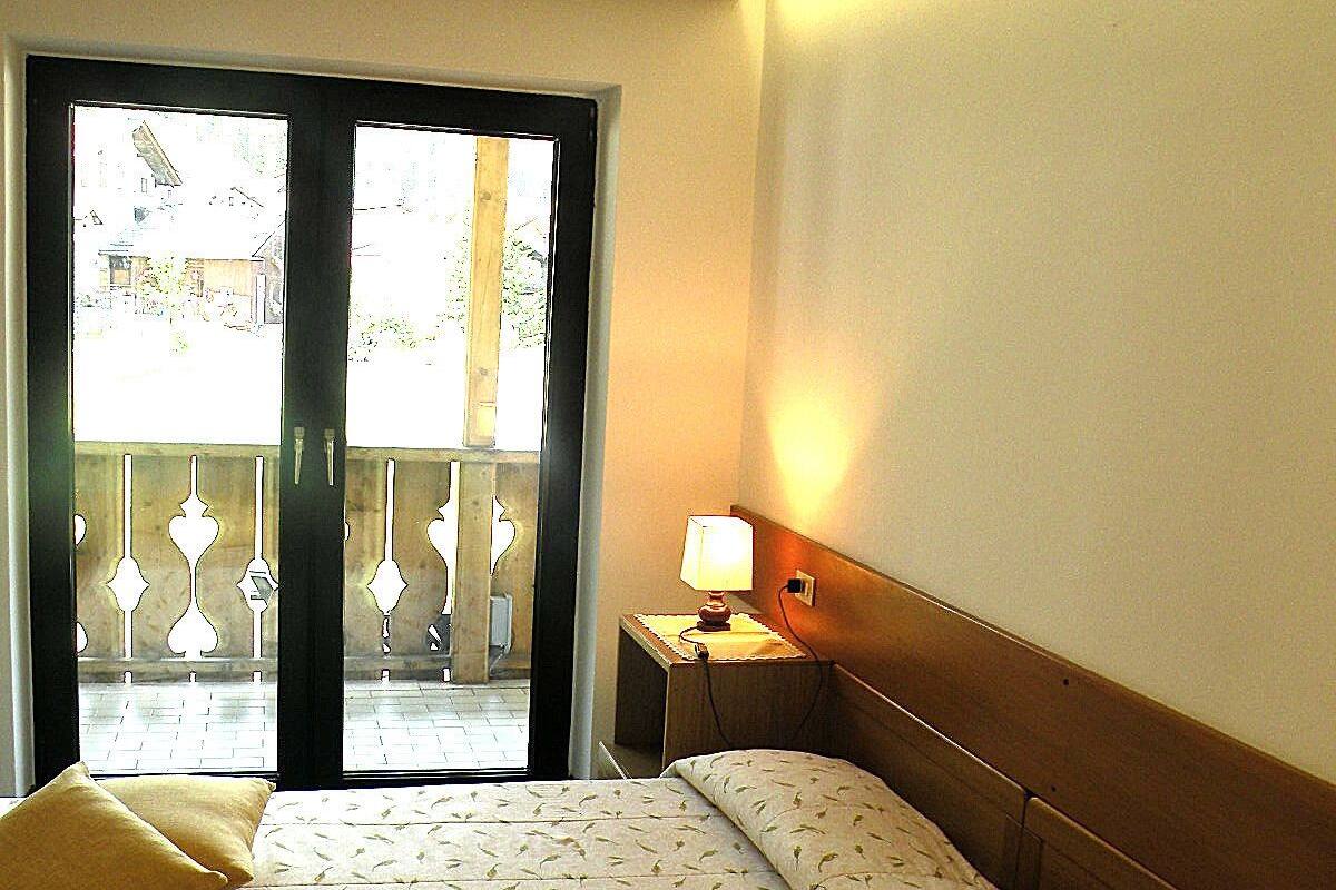 A hotel room with a bed, a nightstand with a lamp, and a view through a glass door.
