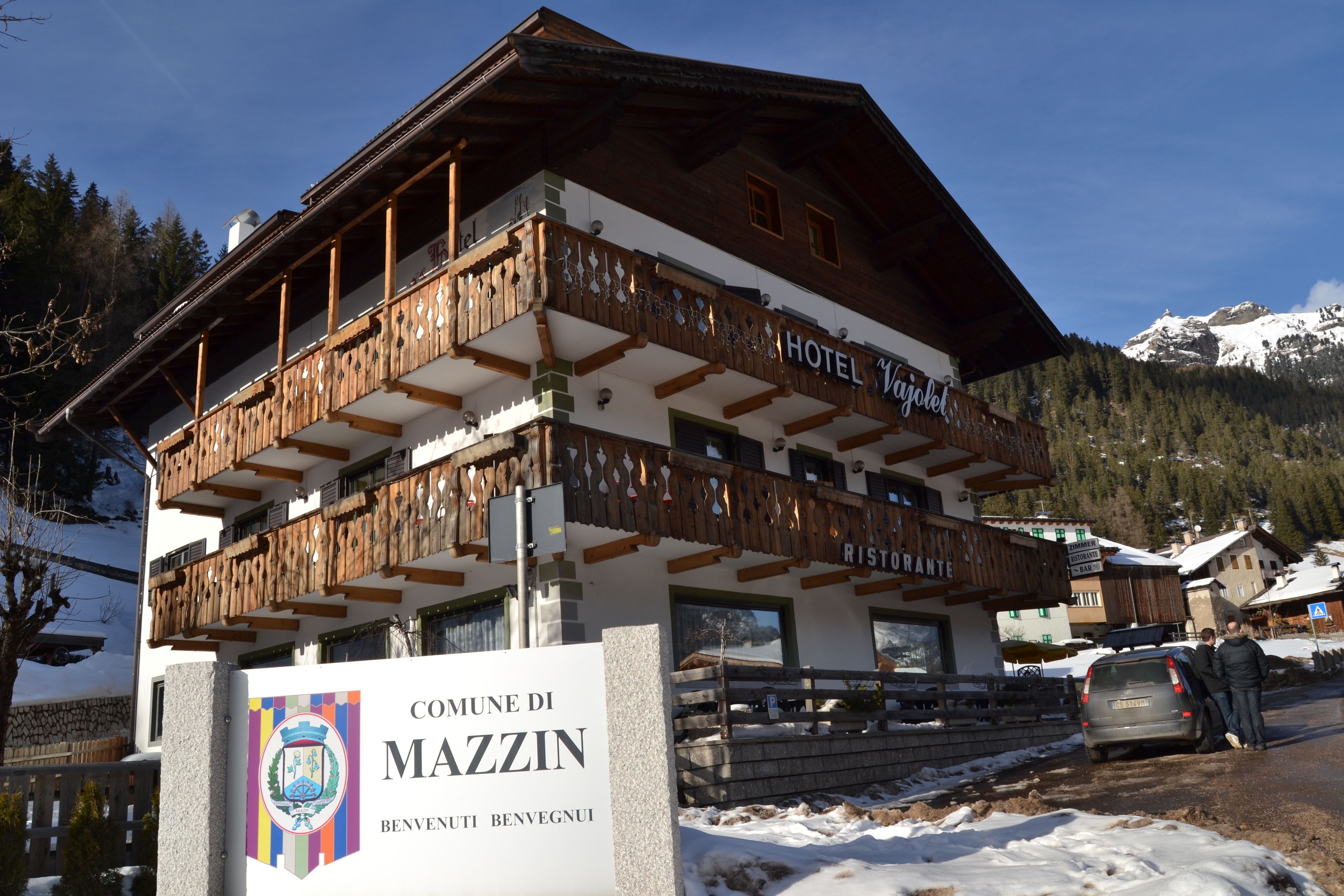 Un hotel con fachada de madera, balcones y un cartel que indica que se encuentra en el Comune di Mazzin.