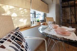 Un comedor con mesa de vidrio, mantel blanco y una silla de mimbre.