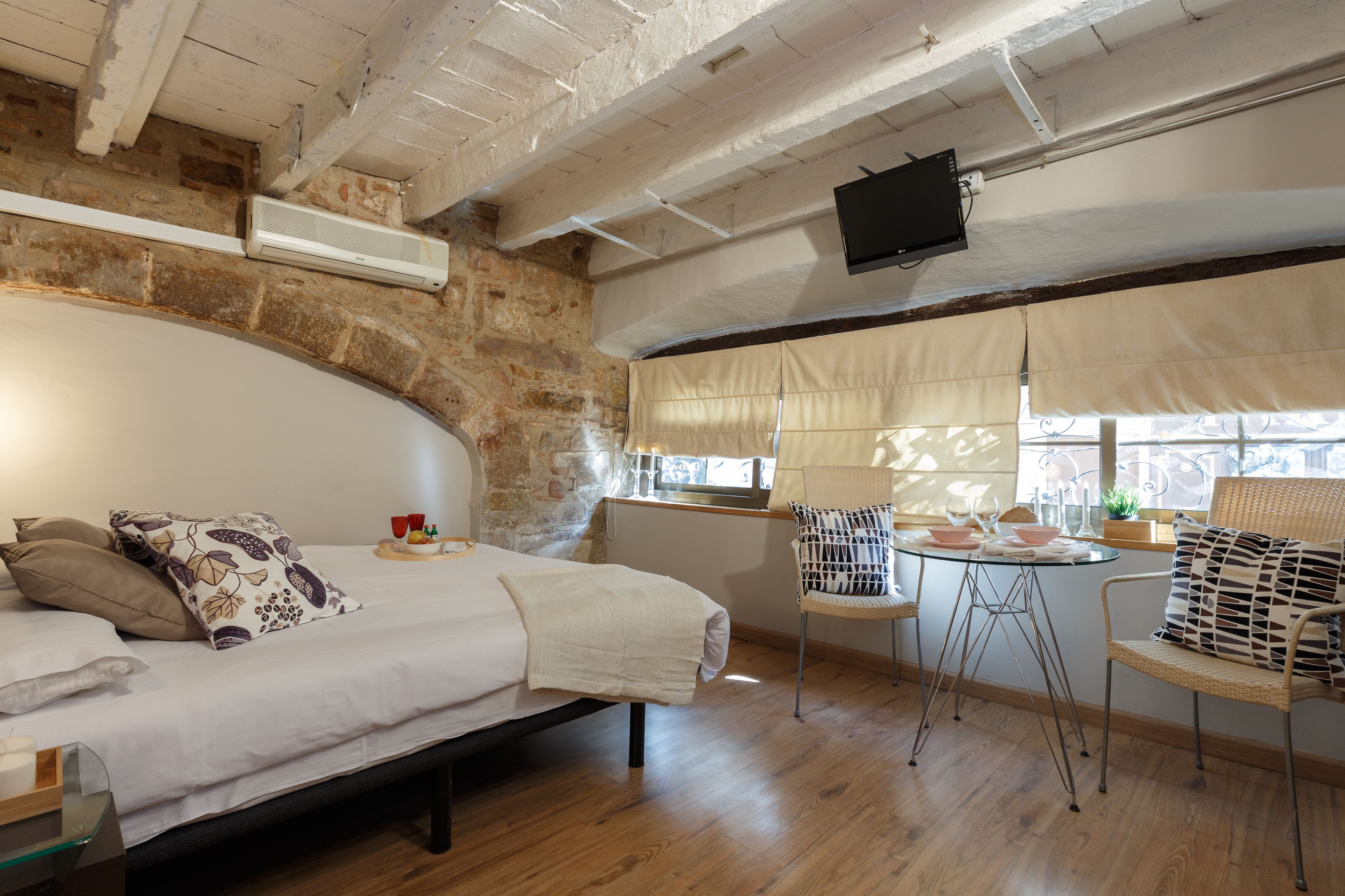 Une chambre à coucher comprenant un lit, une chaise, une petite table et un téléviseur fixé au mur.